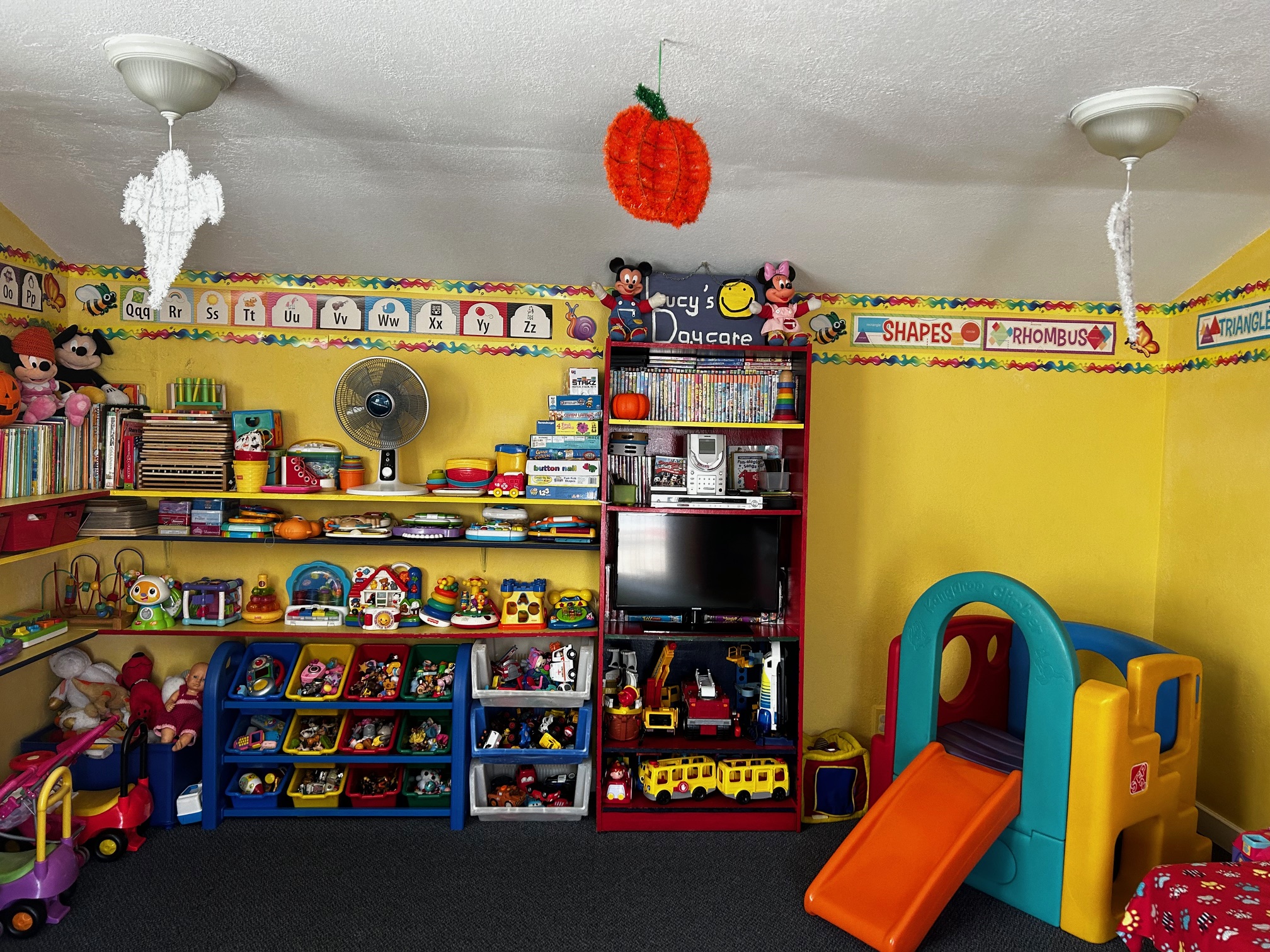 A side of the daycare with a TV, toys, a TV, and a small playstructure.